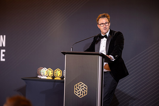 Keith Smith, CEO of HRUC speaking on stage behind a lectern at the National Innovation Challenge awards ceremony. He is wearing a tuxedo.
