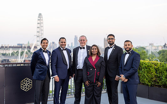 NIC's 2026 panel of independent judges - Amazon Senior Chief Engineer Thiloshini Ellary-Bachu, BT Sustainability Director Sarwar Khan, MIT ILP Director Steve Whitaker, The Education Space chief executive Iqbal Vaza, and Director of One Care IT Pally Randhawa. All dressed in formal wear, standing on the terrace of the IET with the London skyline behind them.